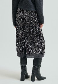 Czarna spódnica z cekinami o fakturowanej powierzchni, z ciemnym wykończeniem. Połączona z czarnymi, skórzanymi kozakami do kolan.