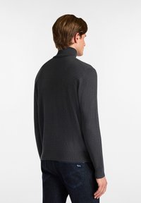 Dunkelgrauer, strukturierter Strickpullover mit hohem Kragen, gerippten Bündchen und Saum. Getragen mit dunklen Jeans, die ein sauberes, minimalistisches Design präsentieren.