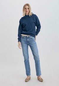 Felpa blu navy con una finitura texture, abbinata a jeans in denim blu chiaro. Il modello si erge con sicurezza, mostrando l'outfit informale.