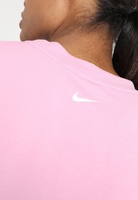 Camiseta de algodón rosa con cuello redondo y un pequeño logo blanco de Nike en la espalda, que muestra una textura suave y lisa.