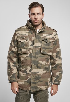 Veste de camouflage dans des tons de vert et de marron, avec quatre poches avant, un col haut et des cordons de serrage réglables à l'ourlet.