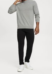 Šedý pletený svetr s kulatým výstřihem, zkombinovaný s černými slim-fit džíny a bílými teniskami, což podtrhuje ležérní outfit.