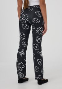 Pantaloni neri a campana con motivi floreali bianchi e farfalle, realizzati in tessuto morbido, dotati di vita alta e cucitura centrale sul retro.