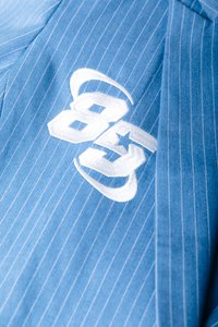 Ύφασμα με μπλε ρίγες και λευκή κέντημα που απεικονίζει τους αριθμούς «85» και ένα αστέρι. Απλός, ραμμένος σχεδιασμός με ομαλή υφή.
