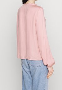 Blusa rosa chiaro con maniche lunghe e scollatura a volant, realizzata in un tessuto morbido, abbinata a jeans in denim a vita alta.