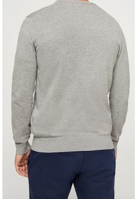 Pull gris en maille avec manches longues, col rond et poignets côtelés. Semble doux et texturé, porté avec un pantalon bleu marine.