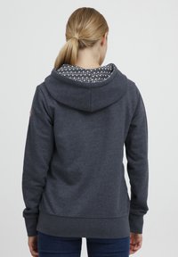 Hoodie gris foncé avec une doublure intérieure texturée et à motifs dans la capuche. Il possède des manches longues et une coupe décontractée. Tissu doux avec un ourlet côtelé.