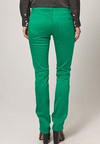 Groene denim jeans met een slim fit, voorzien van achterzakken en een gladde textuur. G gedragen met zwarte stiletto hakken en een donkere top.