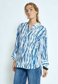 Camicia a maniche lunghe blu e bianca con un colletto, caratterizzata da una vestibilità rilassata e trame a righe. Abbinata a jeans in denim.