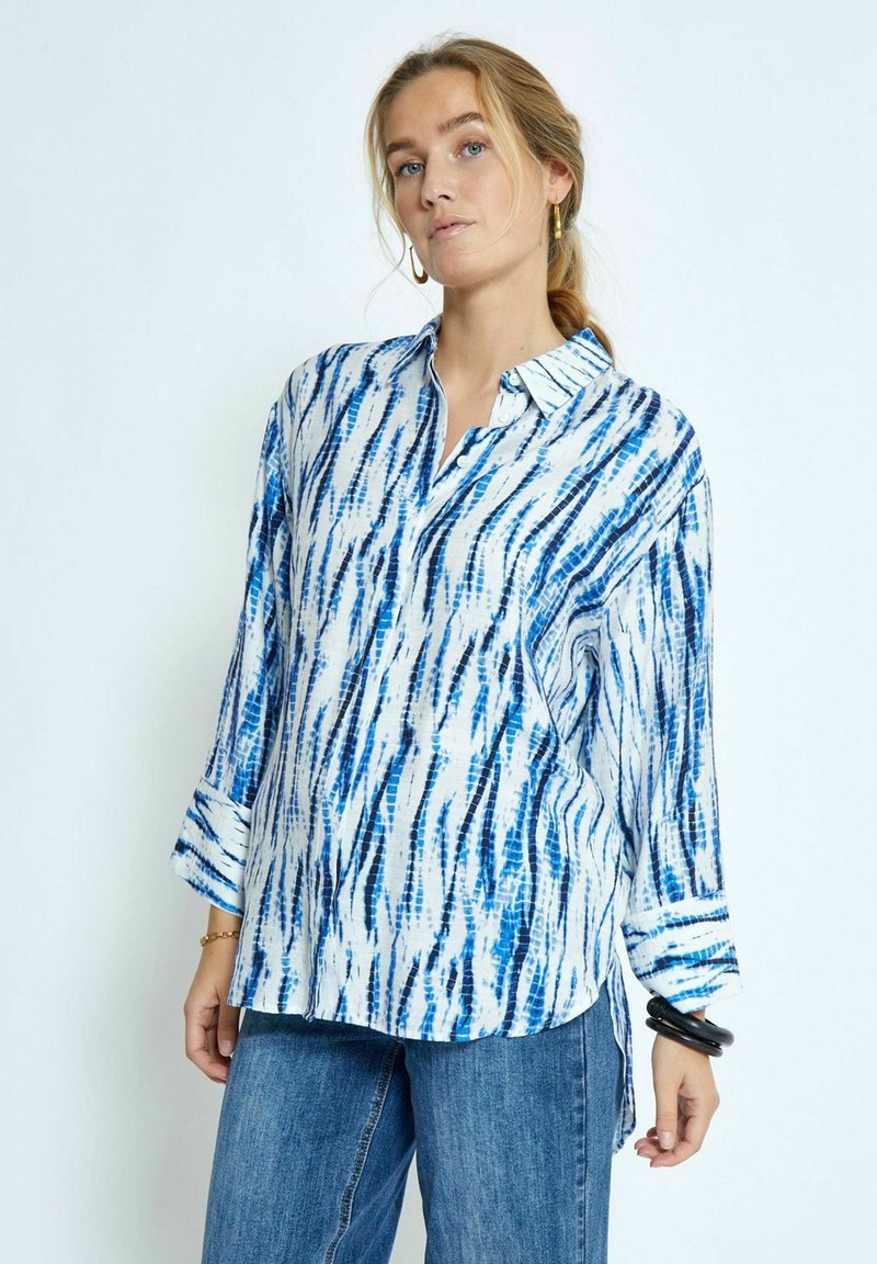 Camicia a maniche lunghe blu e bianca con un colletto, caratterizzata da una vestibilità rilassata e trame a righe. Abbinata a jeans in denim.