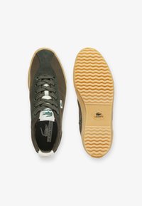 Sneakers verde in suede con dettagli testurizzati, lacci bianchi e suola in gomma. La suola presenta un motivo ondulato e il logo Lacoste.