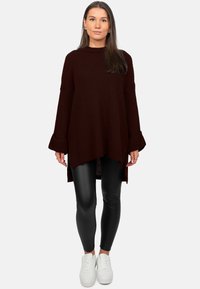 Maglione oversize color bordeaux con trama a coste, maniche lunghe, spacco ai lati, abbinato a leggings neri e sneaker bianche.