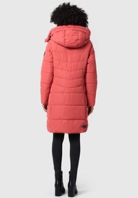 Garšs puffer mētelis korallkrāsā, ar kapuci, quilted dizainu un logo detaļu apakšmalā. Apvienots ar melnām šaurām džinsām un potīšu zābakiem.