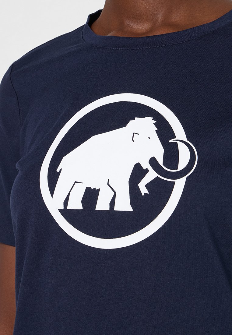 Witte wolharige mammoet symbool binnen een cirkel op een marineblauwe ronde hals t-shirt gedragen door een persoon.