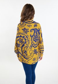 Gebreide poncho in geel met een blauw paisleypatroon, met een hoge kraag en een losse pasvorm, gemaakt van zachte, gestructureerde stof.