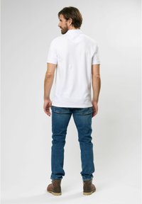 White short-sleeve polo shirt with a collar, paired with blue denim jeans and brown boots. Clean design with no visible patterns or logos.