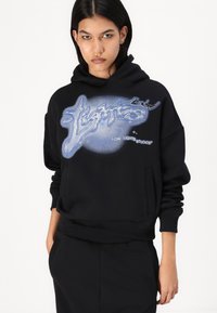 Sweatshirt preto com um design gráfico com detalhes em azul e branco, punhos e bainha canelados, e um bolso tipo canguru para funcionalidade.