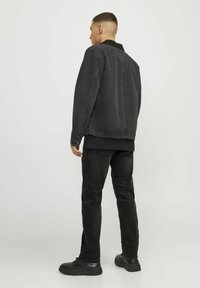 Svart jeansjacka med krage, kombinerad med svarta jeans. Utstyrseln har en avslappnad passform och texturerad tyg, bärs med svarta skor.