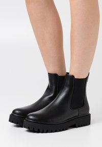Black leather ankle boots with elastic side panels, chunky rubber soles, and a smooth texture. Features a rounded toe and minimal stitching.