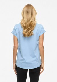 T-shirt in cotone azzurro chiaro con maniche arrotolate, scollatura rotonda e orlo curvo. Indossata con jeans neri, vista da dietro.