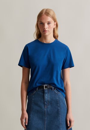Blaues Baumwoll-T-Shirt mit Rundhalsausschnitt, kurzen Ärmeln und leicht fallenden Schultern, kombiniert mit einem Jeansrock und einem schwarzen Gürtel.