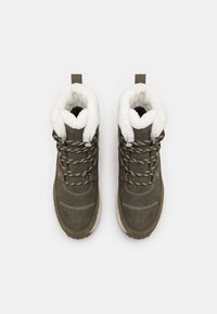 Grønne sueboots med hvit faux pelsfôr, lys beige såle og svart-hvite mønstrede snørebånd. Har forsterkede hull og merker.