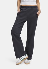 Mørkegrå joggebukser med bred ben-design, som har elastisk liv og sidelommer, parret med grønne og hvite sneakers.