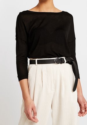 Maglione nero, leggero, con scollo a barca largo, abbinato a pantaloni plissettati color crema a vita alta e una cintura nera.