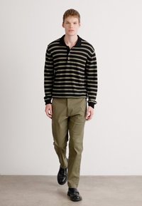Polo cu dungi negre și măsline, cu mânecă lungă și guler, asortat cu pantaloni de culoare măslinie și pantofi negri; textură netedă, croială relaxată.