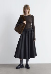 Brown long-sleeve top, black ankle-length skirt, black loafers, gray socks, and a brown fur-accented bag. Minimalistic design and neutral colors.