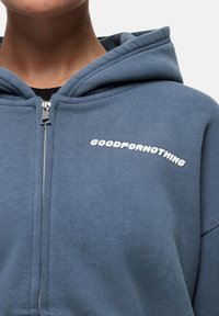 Felpa con cappuccio in blu ardesia, dotata di una cerniera frontale e di testo bianco "GOODFORNOTHING" sul petto. Tessuto morbido in misto cotone.