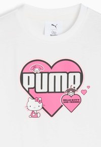 Biała koszula z dużym różowym logo serca, napisem "PUMA" oraz postaciami z kreskówek Hello Kitty i przyjaciół otaczającymi dwa mniejsze serca.