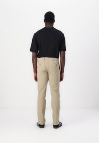 Pantalon beige à coupe droite, fabriqué en tissu doux. T-shirt noir à manches courtes, vu de dos, avec des chaussures décontractées.