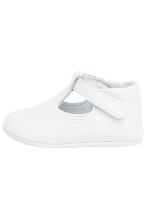 Chaussure Mary Jane en cuir blanc avec un design découpé, une sangle sur le cou-de-pied et des coutures visibles le long de la semelle. Texture lisse.