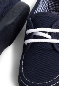 Marineblaue Leinenschuhe mit weißen Schnürsenkeln, Gummisohlen und kontrastierendem hellen Nähen. Das Innere weist ein kariertes Muster auf.