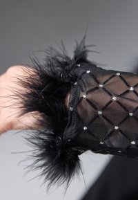 Tejido negro transparente con adornos en patrón de diamante y un acabado de plumas negras en los puños, con dos botones redondos negros.