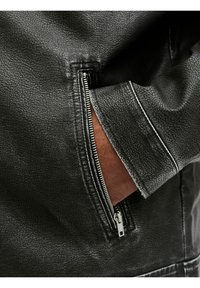 Mustapronen takki, jossa on teksturoitu pinta, vetoketjullinen tasku ja kontrastivärinen valkoinen ommel hihassa.