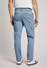 Light blue cargo pants with back pockets and side cargo pockets, made of cotton. Styled with white shoes featuring black accents.
