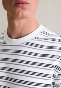 Gestreiftes Baumwoll-T-Shirt mit weißem Grund, das horizontale Linien in Marineblau, Lavendel und Helllila zeigt. Rippbündchen am Rundhalsausschnitt.