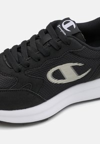 Pantofii sport negri, realizati dintr-un amestec de material mesh si suede, cu o talpa intermediara alba si un logo gri pe partea laterala si pe limba.