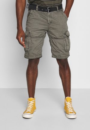 Zielone szorty cargo z wieloma bocznymi kieszeniami, paskiem i luźnym krojem, w połączeniu z żółtymi wysokimi trampkami.