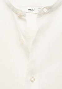 Chemise en lin blanc avec un col rond bordé de gris et deux boutons transparents à l'avant. Texture douce, design minimaliste.