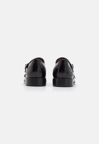 Black leather shoes with a polished finish, featuring a classic silhouette, brogue detailing, and a low stacked heel.