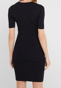 Abito bodycon nero a coste con maniche corte, silhouette aderente e lunghezza sopra il ginocchio. Presenta un collo rotondo e una texture liscia.