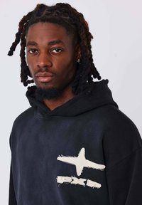 Sudadera con capucha negra que presenta acentos gráficos desgastados en blanco en el pecho, hecha de una tela suave con un corte relajado y cordón ajustable.