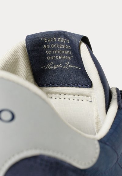 Wewnętrzny język buta z przyszytą granatową tkaninową metką z cytatem: „Każdy dzień to okazja, by się na nowo wynaleźć.”