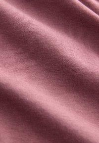 Blødt, ribbet stof i en afdæmpet rosafarve, der viser en glat tekstur med ensartede syninger og en let glans over hele overfladen.