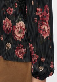 Svart plissert bluse med store røde og rosa blomstertrykk, myk, teksturert finish og ballongerm.