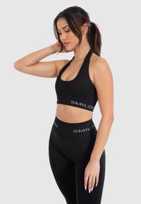 Zwarte sportieve crop top met een ronde halslijn en racerback ontwerp, gecombineerd met hoge zwarte leggings met een logo band.