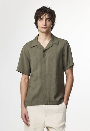 Olijfgroene shirt met korte mouwen van een gemêleerde stof, met een ontspannen pasvorm en een uitgesneden kraag. Draagt met lichte, fijne broek.